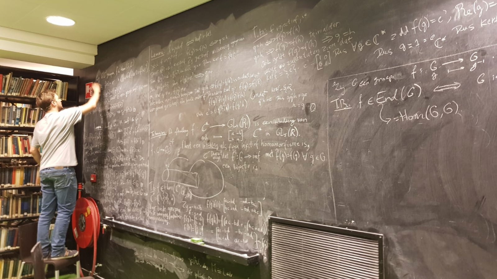 Jos schrijft bovenaan een krijtbord vol abstracte algebra